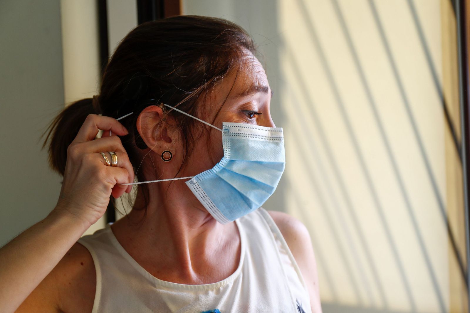 Loli, profesora, usuaria de un implante coclear y miembro de FIAPAS (Confederación Española de Familias de Personas Sordas), se coloca una mascarilla intentando que no se le enganche con el implante