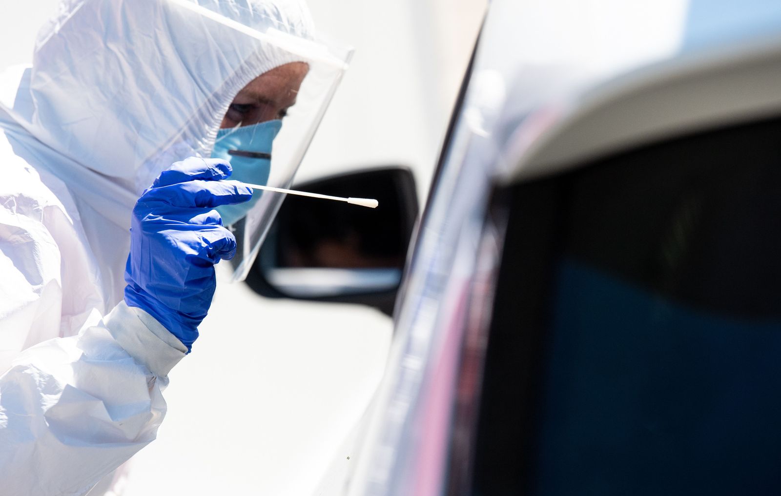 30 July 2020, Bavaria, Bergen: A health worker dressed in Personal Protective Equipment (PPE) takes a smear test from a car driver at a coronavirus (COVID-19) test centre on the motorway 8 (A8) at the