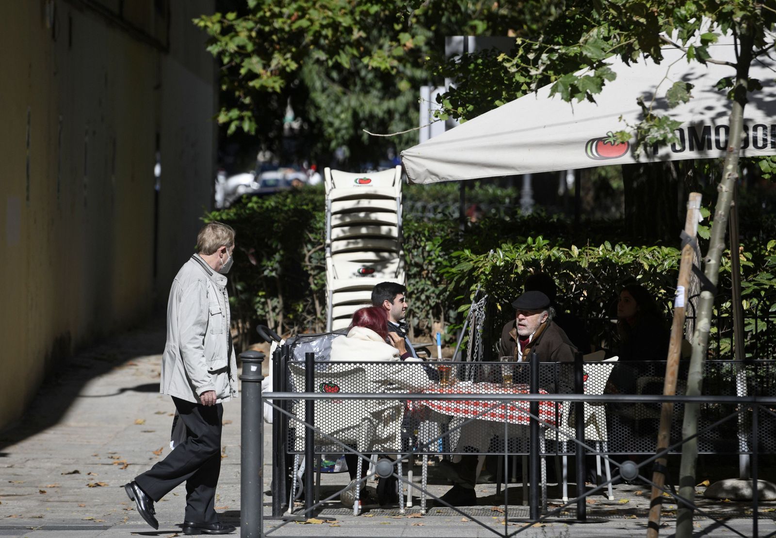Un hombre camina frente a la terraza de un bar donde hay sentadas otras tres personas en la zona básica de salud de Guzmán el Bueno, en el distrito de Chamberí, en Madrid (España), a 26 de octubre