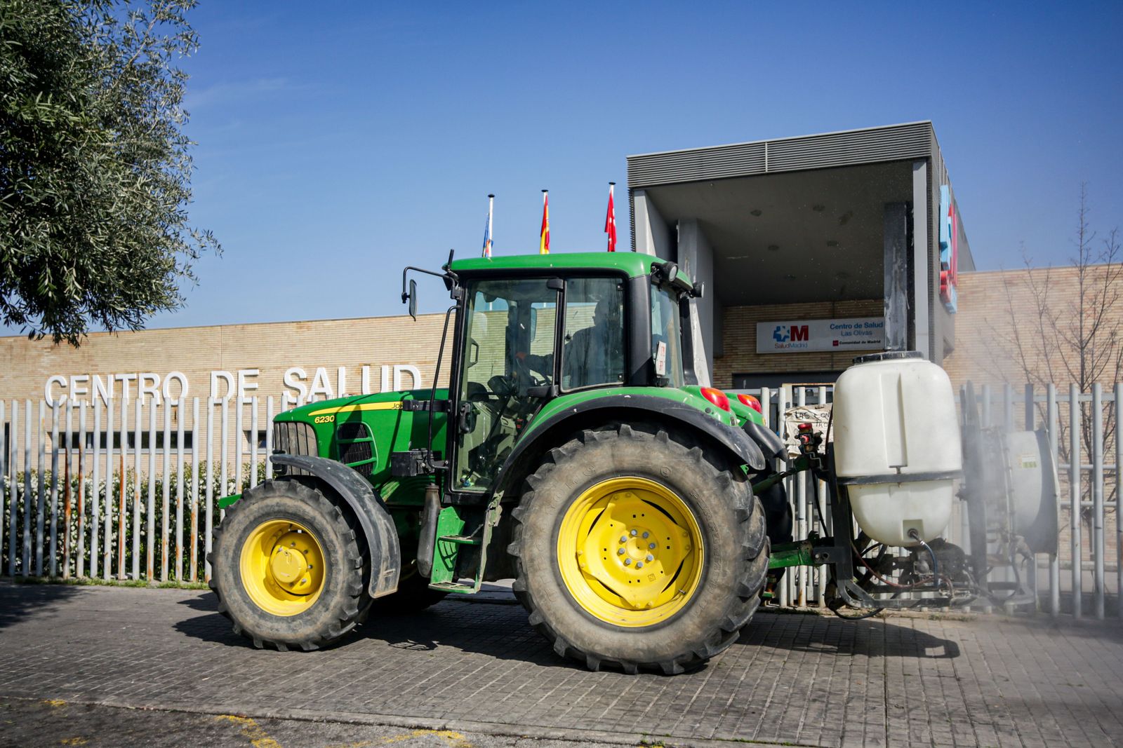 Un agricultor montado en su tractor desinfecta las inmediaciones del Centro de Salud de Aranjuez, dentro del protocolo de actuación activado por la Comunidad de Madrid en el que agricultores de la re