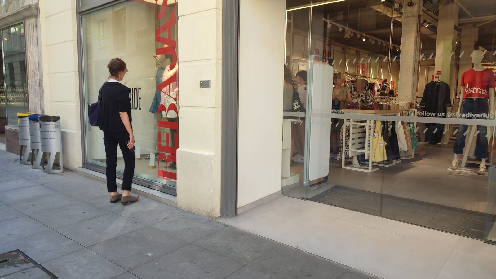 Una mujer mira un escaparate y algunas personas hacen cola en un comercio de Zamora en el primer día de las rebajas de verano