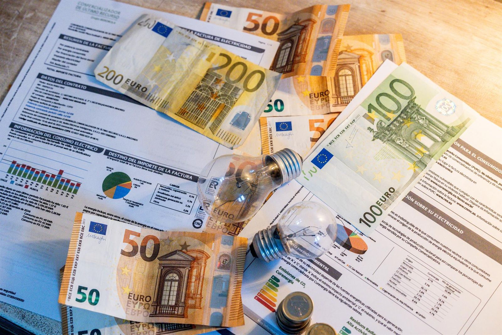 Dos bombillas sobre billetes, monedas y facturas. Ricardo Rubio. Europa Press. Archivo