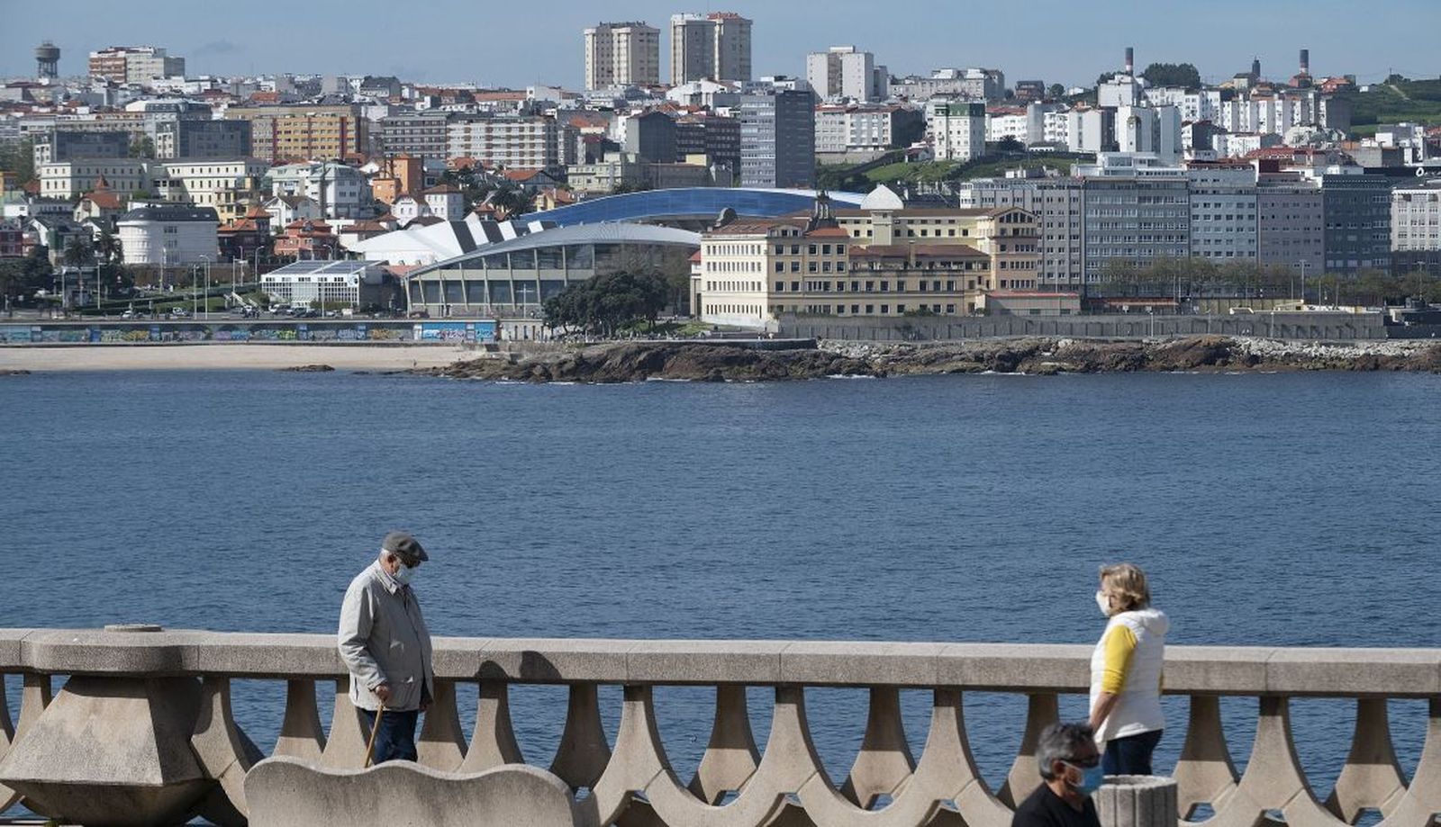 Dos personas pasean por el paseo marítimo de A Coruña, con el estadio de Riazor de fondo