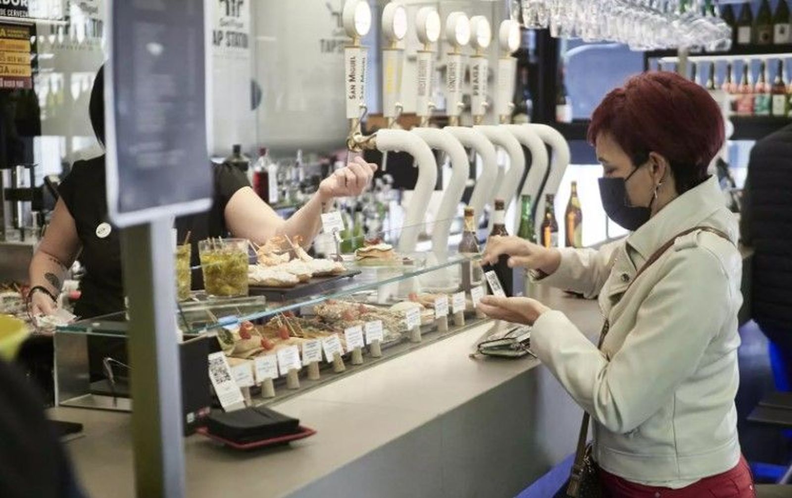 Una mujer con mascarilla se dispone a pagar en un bar. EP