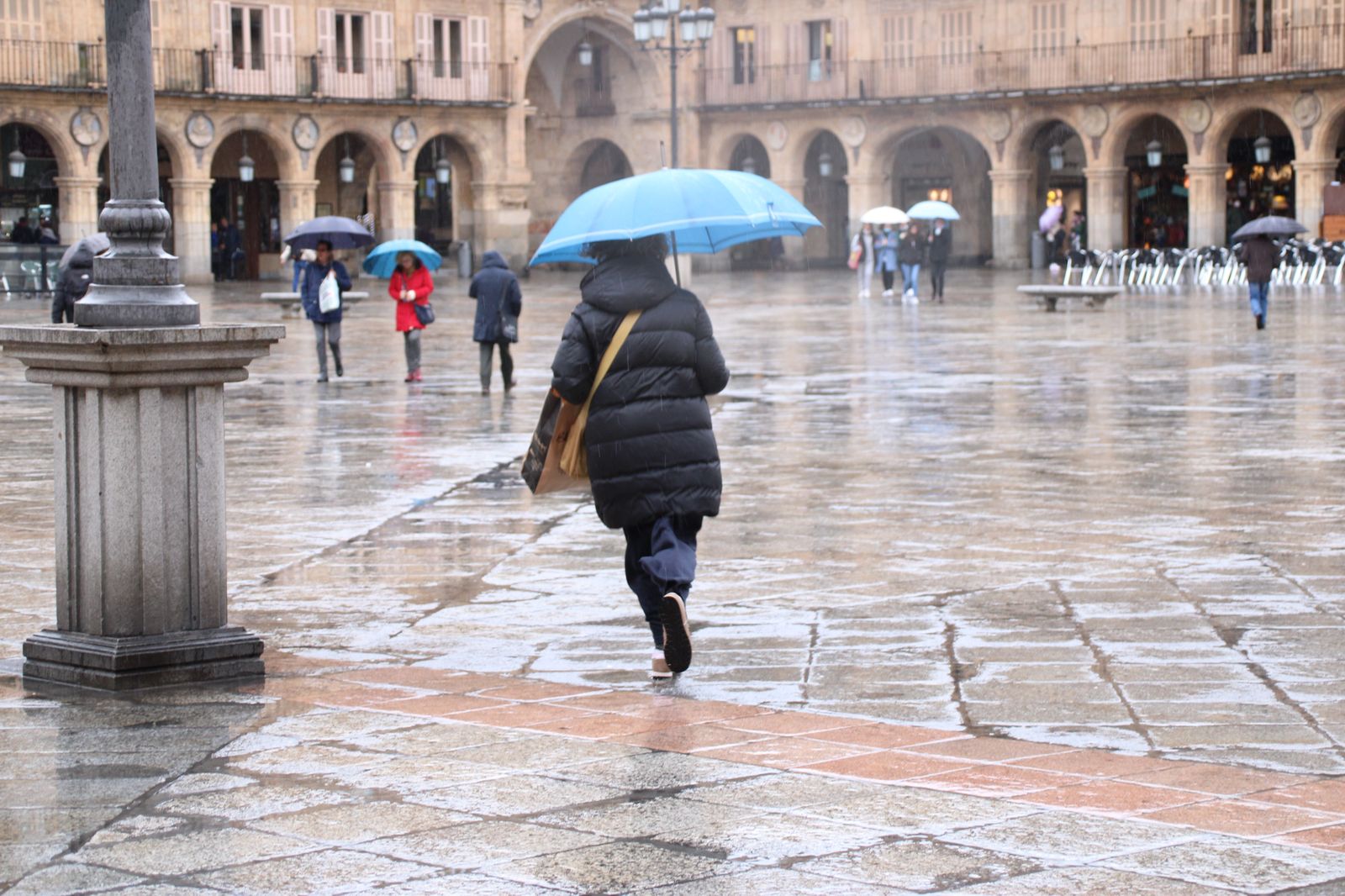 Mujer corre bajo la lluvia en la Plaza Mayor