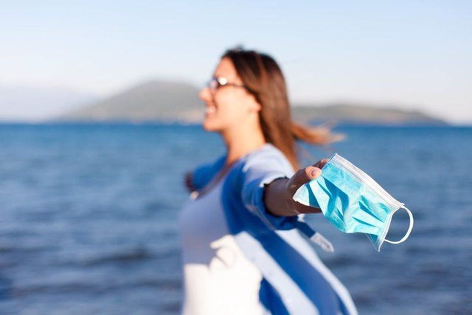 Mujer en la playa con la mascarilla en la mano