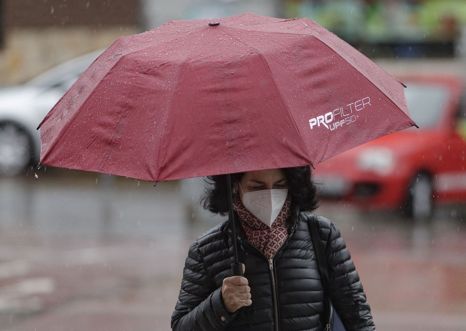 Transeúntes protegidos con mascarilla y un paraguas caminan por las calles de la capital un día marcado por la llegada a la península de una borrasca fría que ha activado la alerta por viento o ll