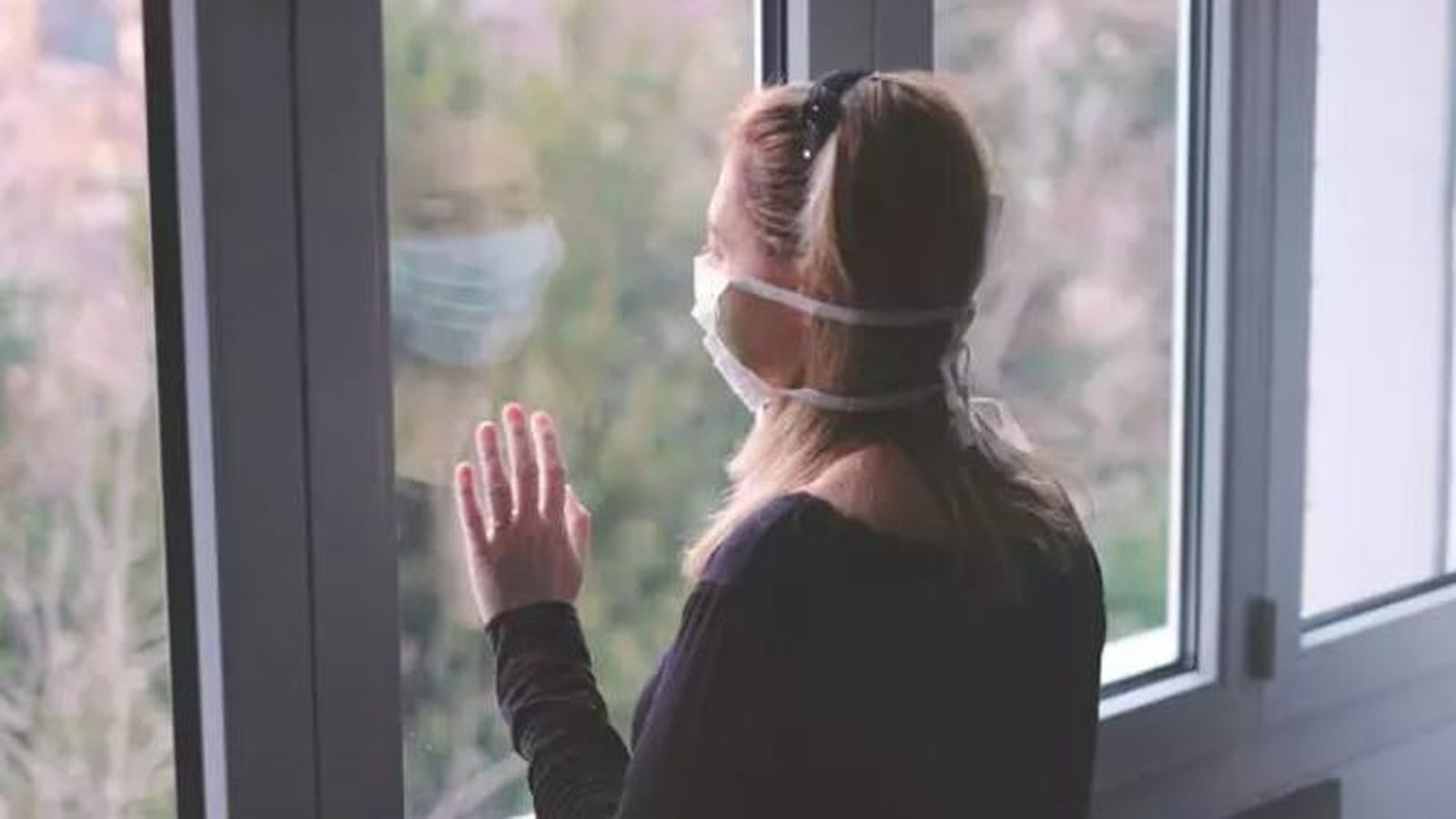 Mujer con mascarilla mira a través de una ventana. Europa Press