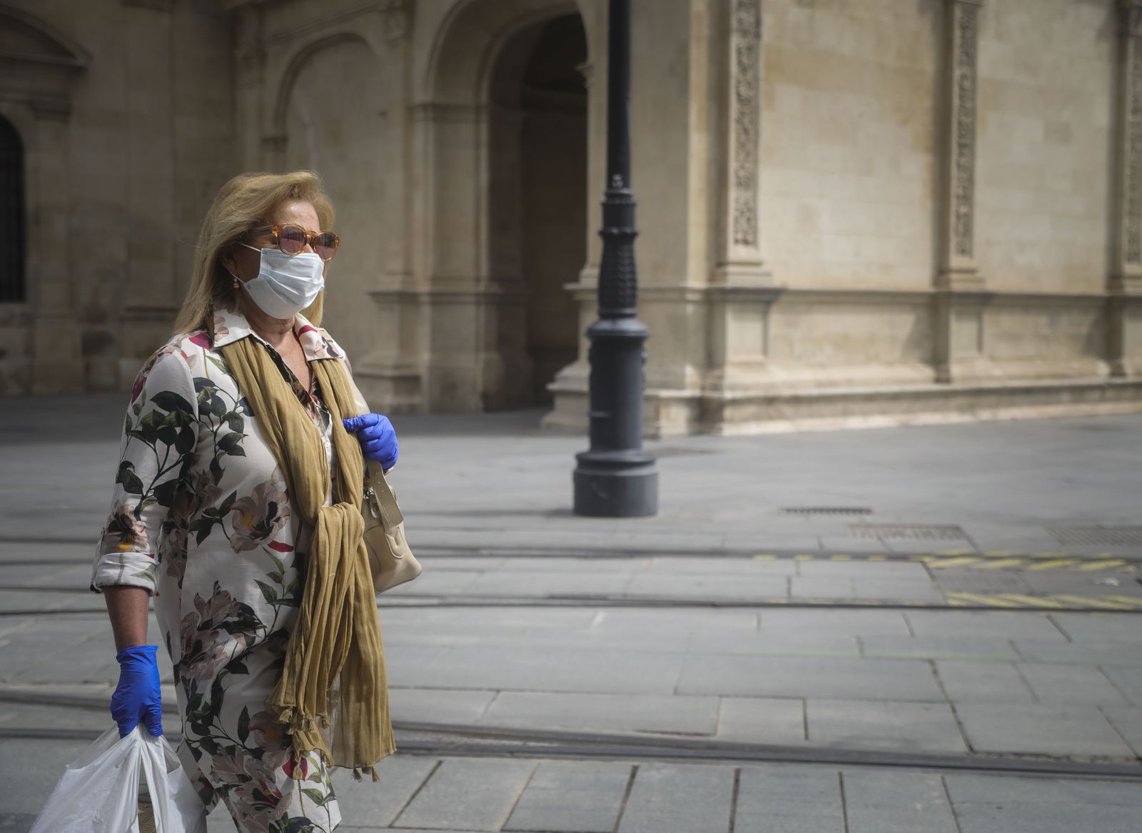 Una mujer caminando protegida con mascarilla y guantes