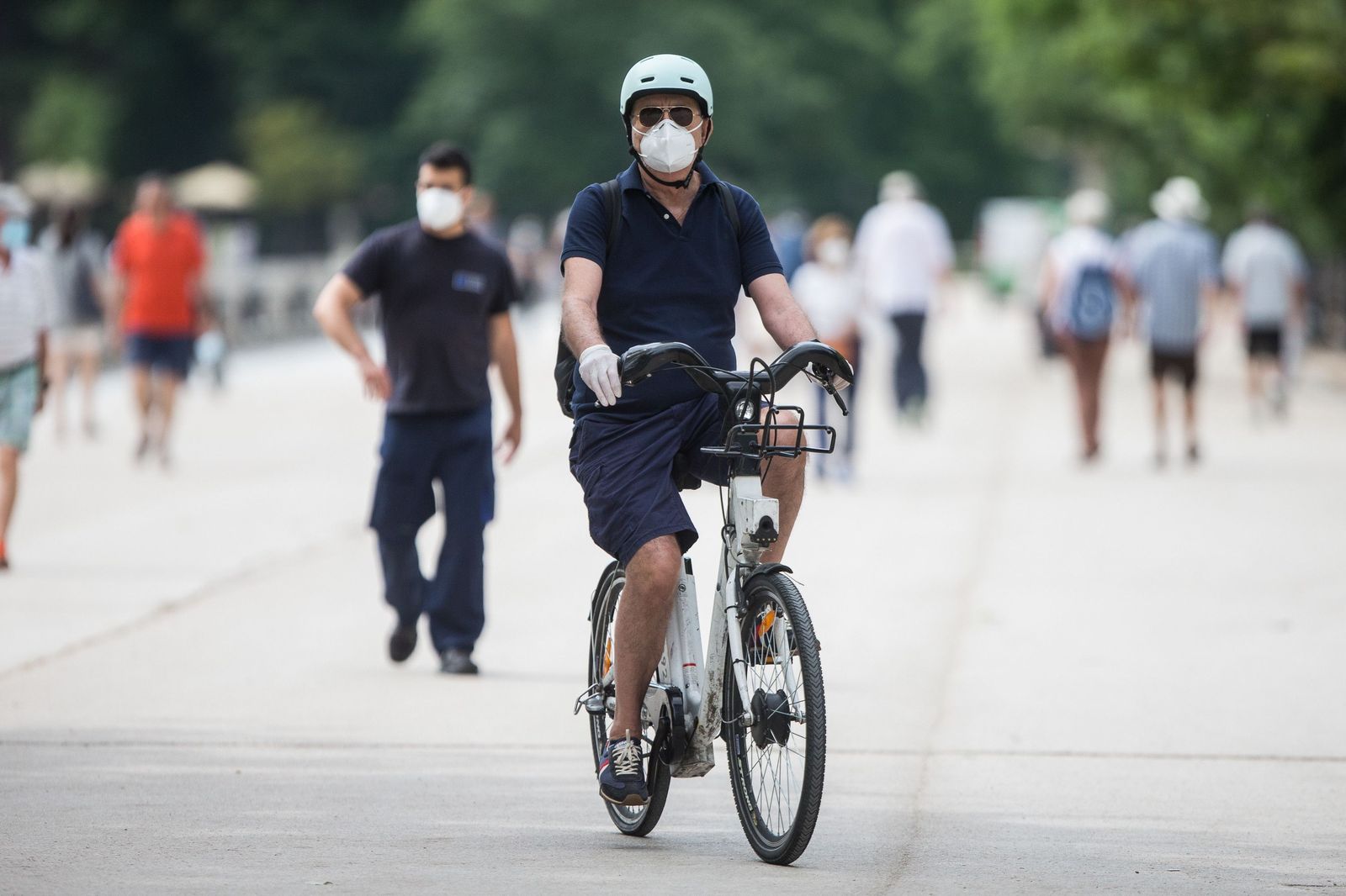 Un hombre protegido con mascarilla y guantes monta en una bicicleta BiciMAD en el parque de El Retiro.