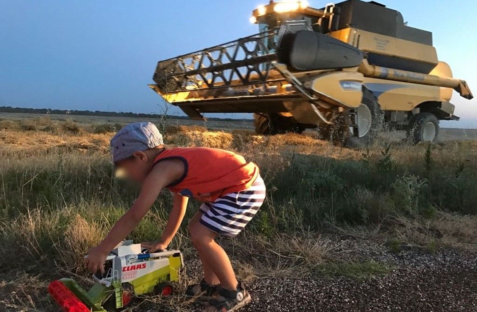 Un niño juega con una cosechadora mientras el padre finaliza la recolección de cereal