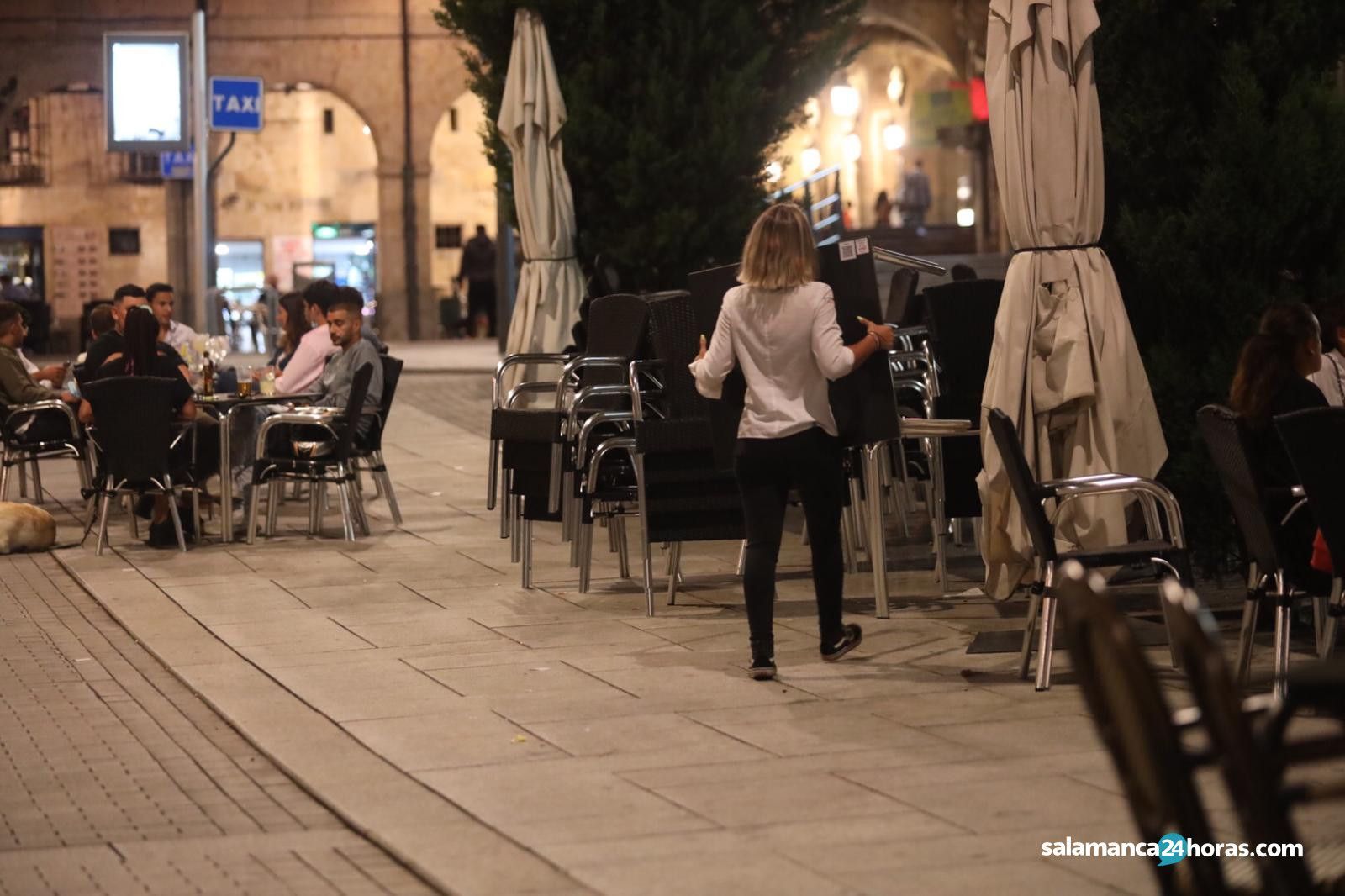 Una camarera recoge las sillas de una terraza en Salamanca.