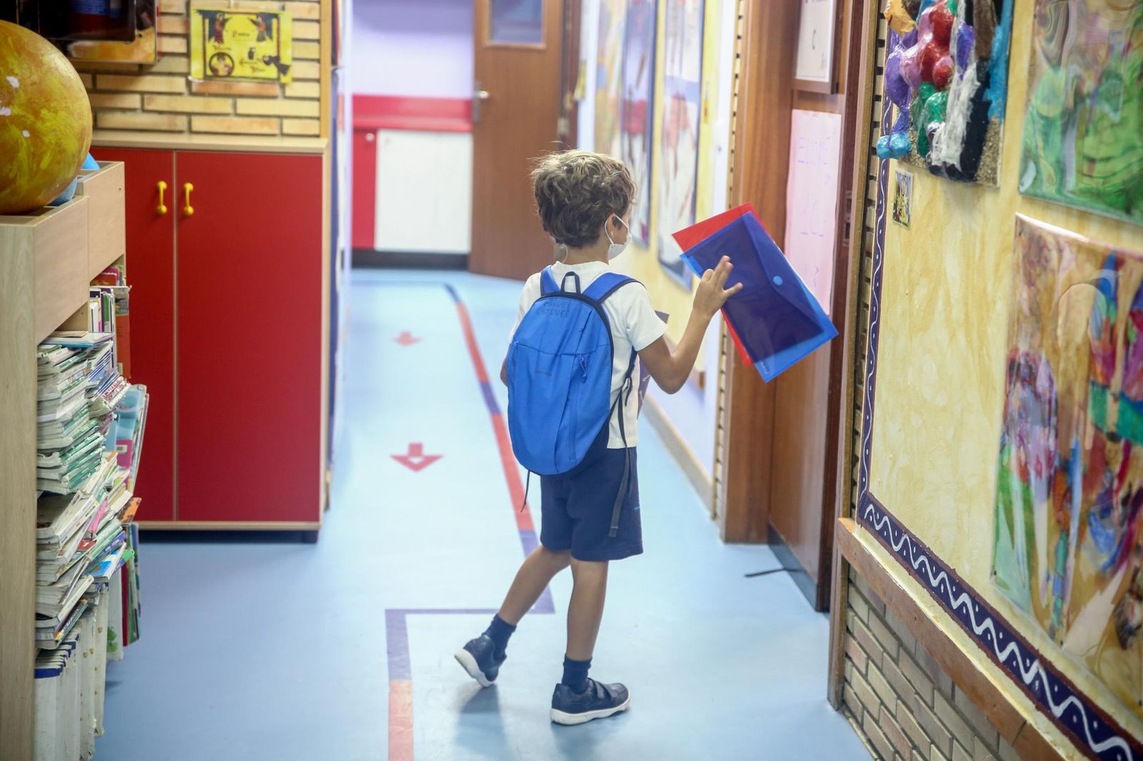 Un niño entrando con su material escolar en el aula