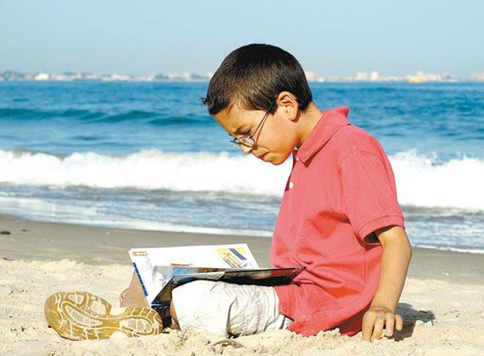 Niño leyendo en la playa | Fotografía Padres y Colegios